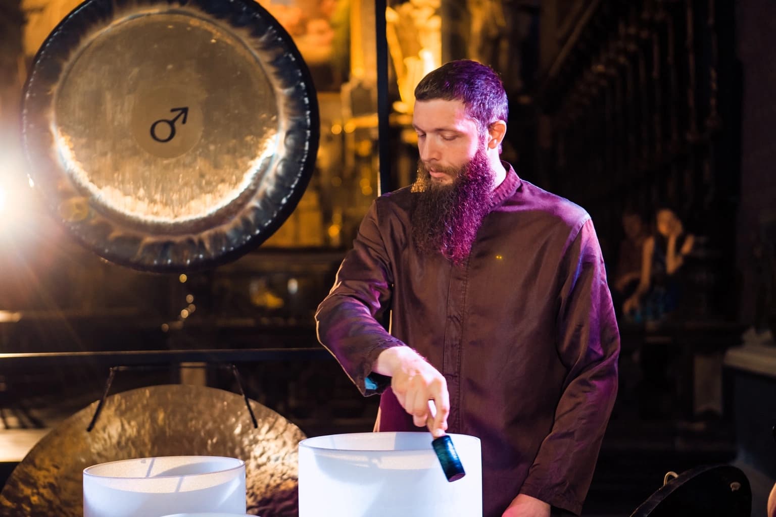 Gong master playing crystal singing bowls beside a large gong